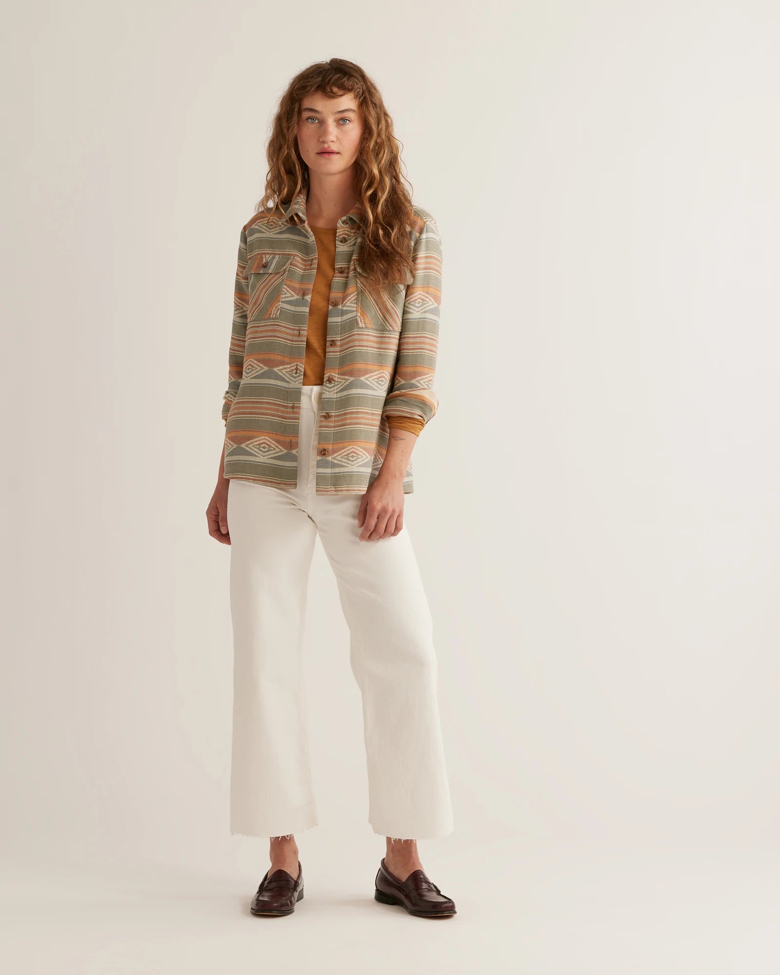 A woman wearing a Pendleton woven shirt with a geometric pattern in tones of beige, green, and brown, paired with white pants.
