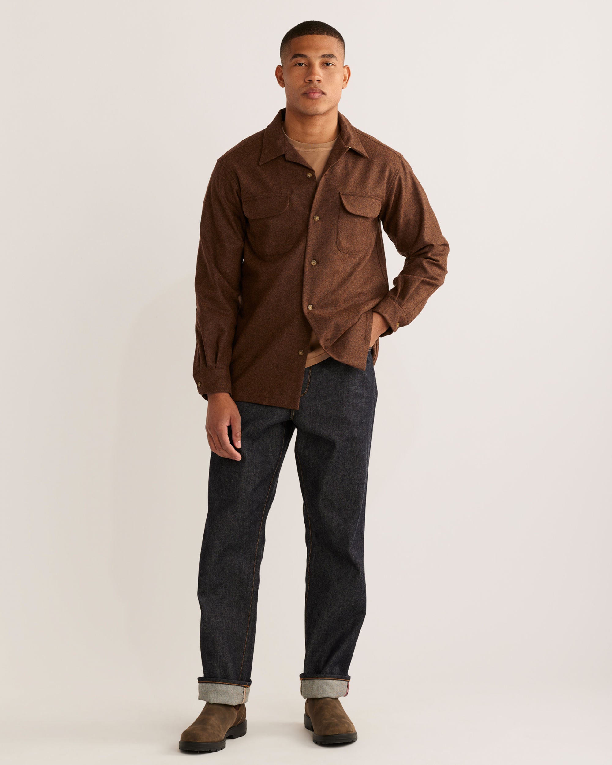 Man wearing a brown shirt and dark jeans on a plain background