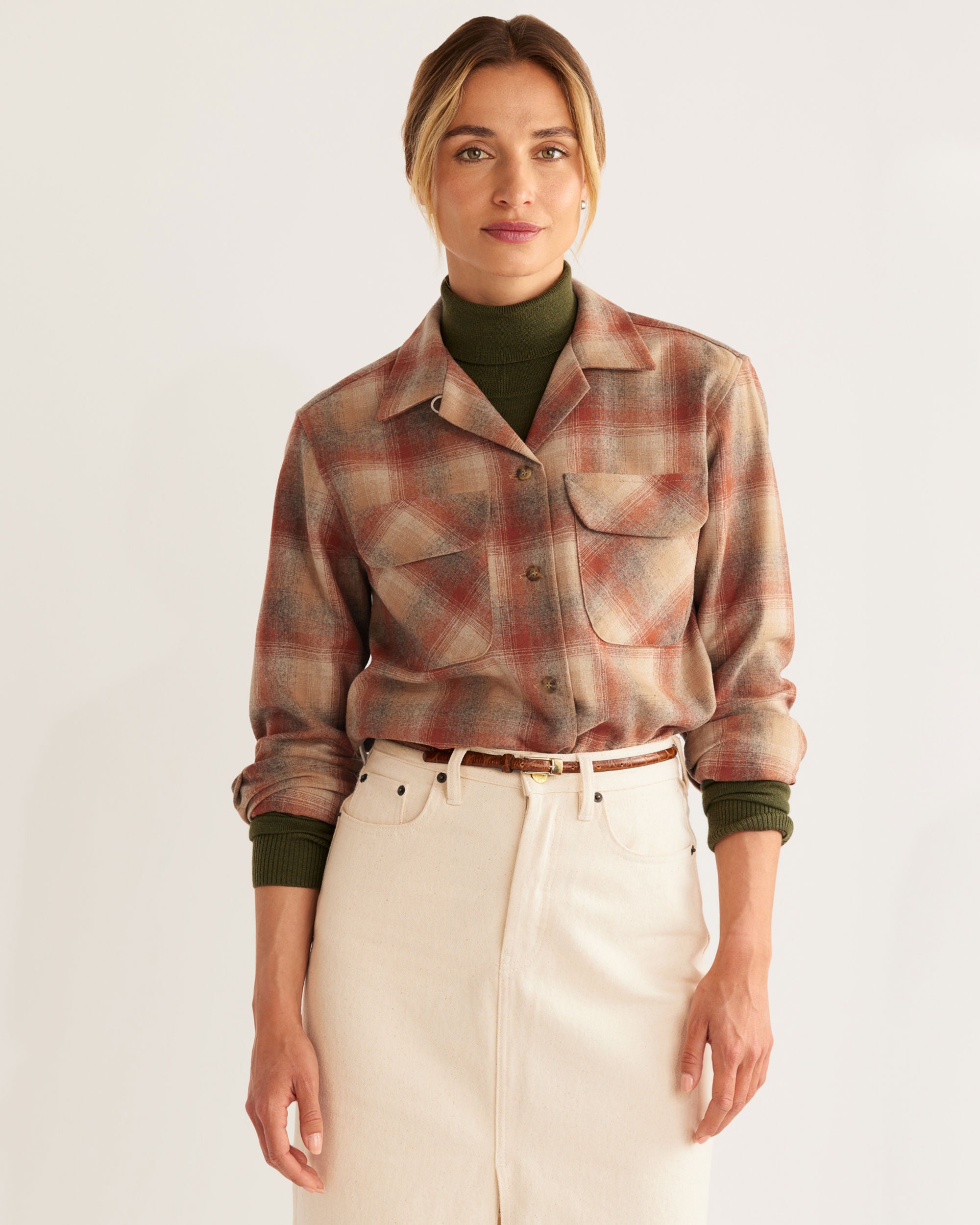 Woman wearing a plaid coat, green sweater, and beige skirt on a white background