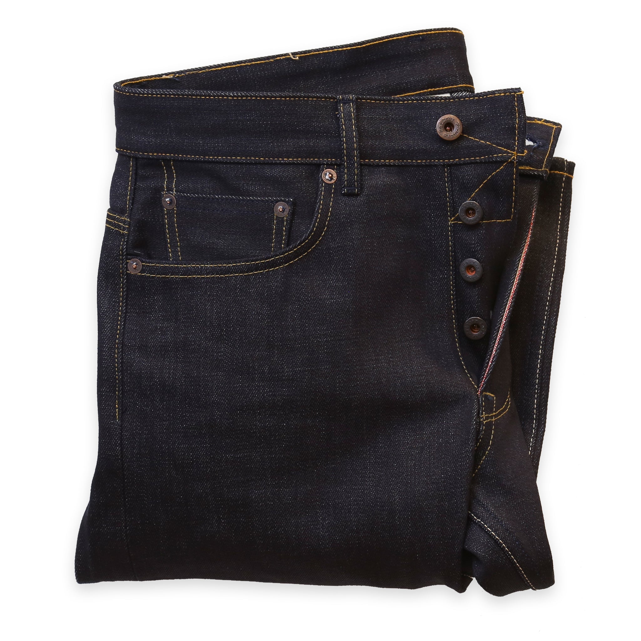 A pair of folded dark denim jeans showing the button replacement service performed on them.