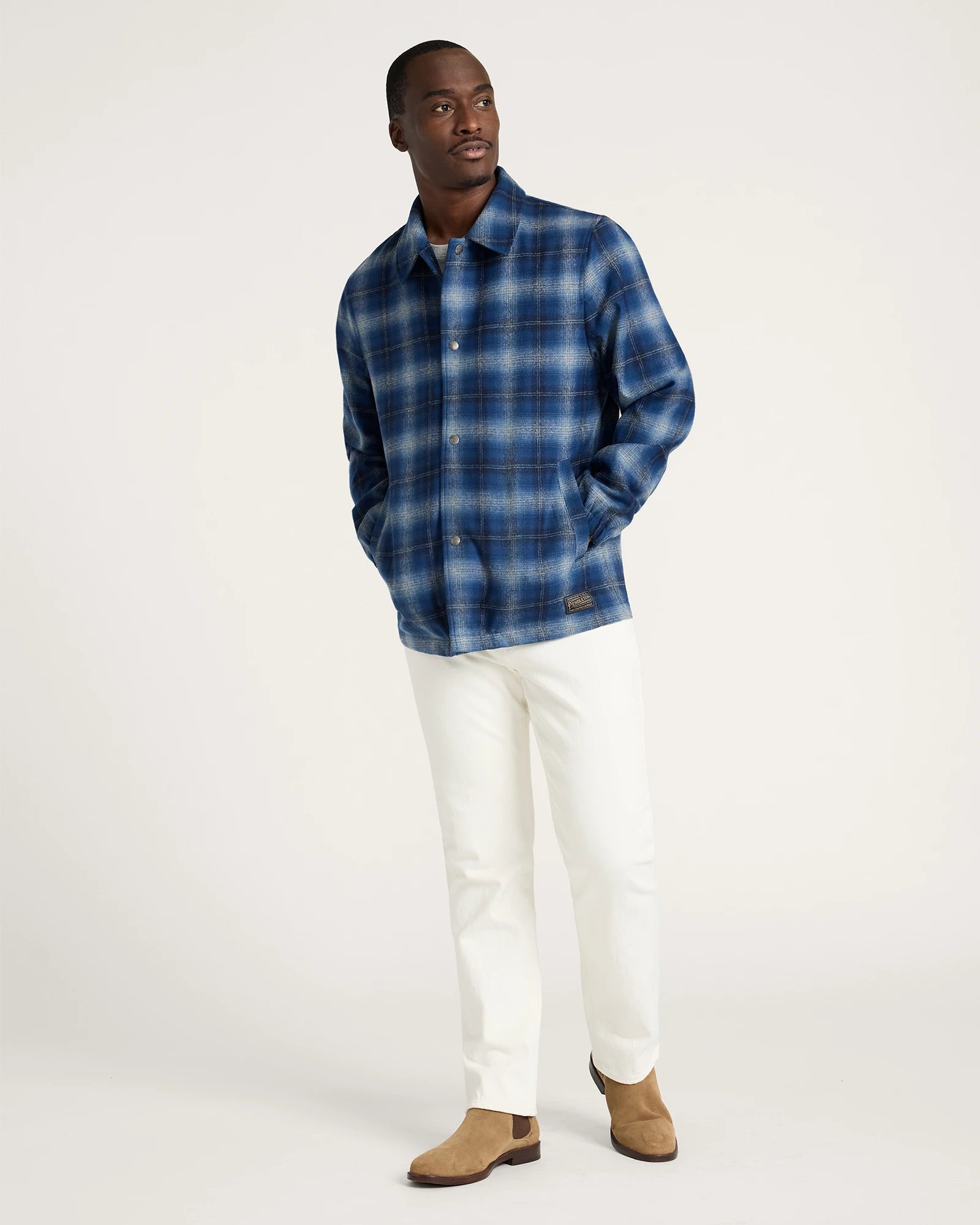 Man wearing a blue plaid shirt and white pants on a white background